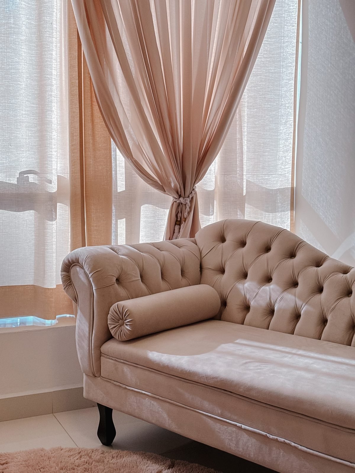 Chaise capitonê clara, que lembra um divã, em uma sala com luz natural