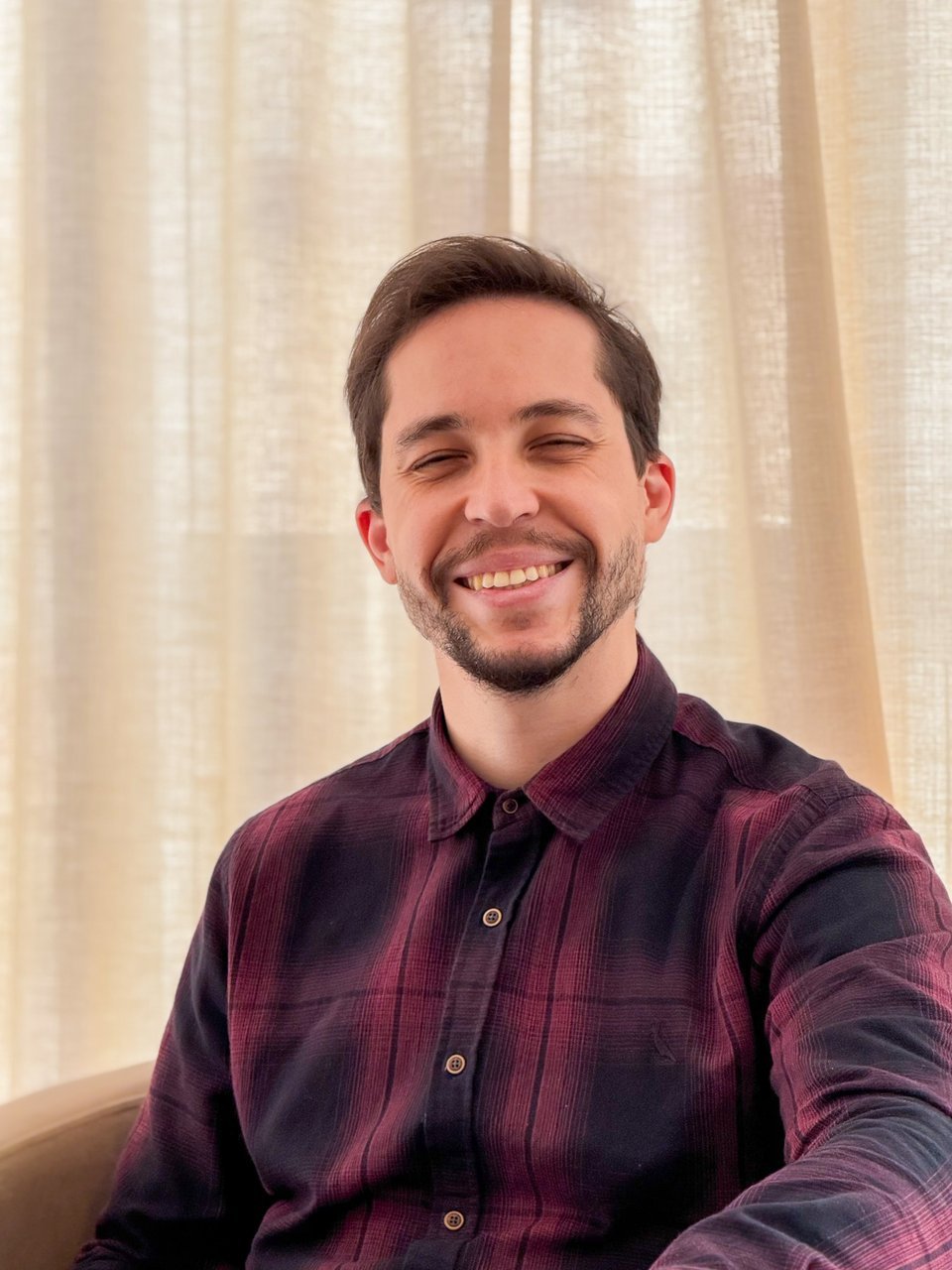 Matheus Vieira da Cunha, psicólogo brasileiro e psicanalista, sorrindo, de camisa xadrez bordô